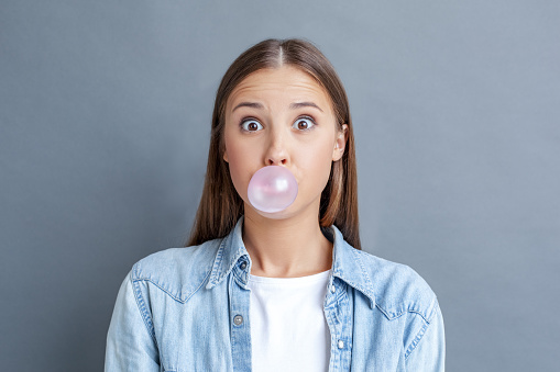 Image of a young woman chewing gum while being surprised, at Surprise Oral & Implant Surgery.
