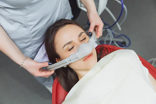 Dental assistant fitting a sedation mask over the nose of her calm female patient at Surprise Oral & Implant Surgery in Surprise, AZ