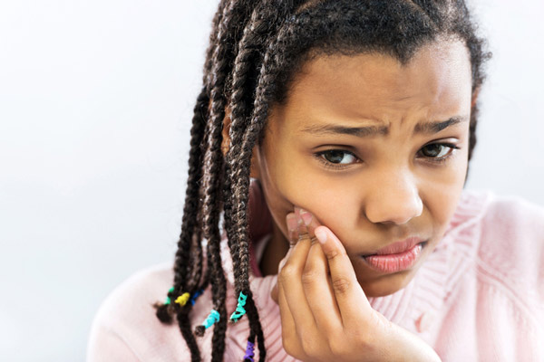 Young girl holding her cheek due to a tooth ache during pediatric dental emergency at Surprise Oral & Implant Surgery in Surprise, AZ