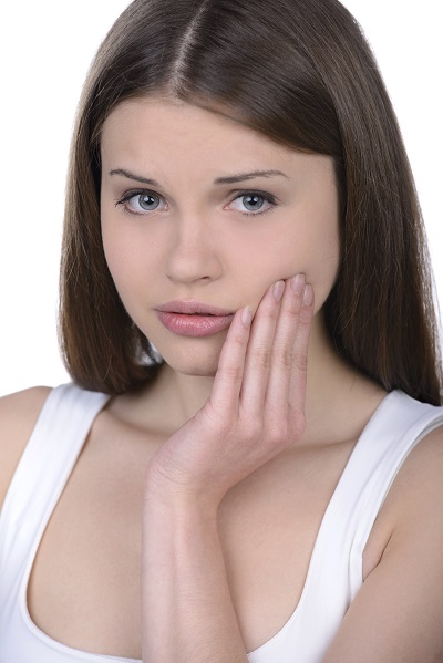 Image of a woman with straight dark brown hair touches face in discomfort.